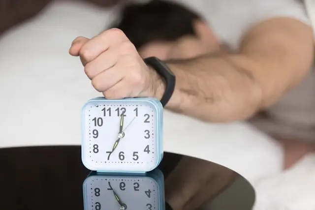 Man in bed hitting his alarm